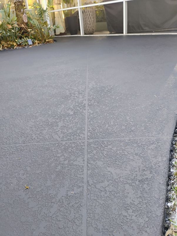 Smooth gray concrete driveway or patio with a curving stone border and garden in the background