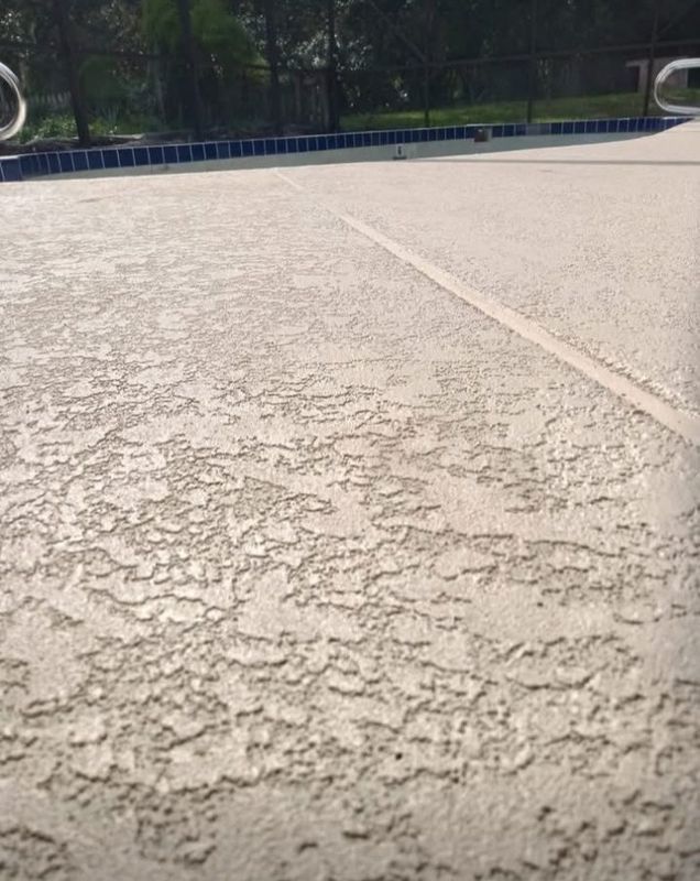 Close-up of a textured concrete pavement with a white line and a blue fence in the background