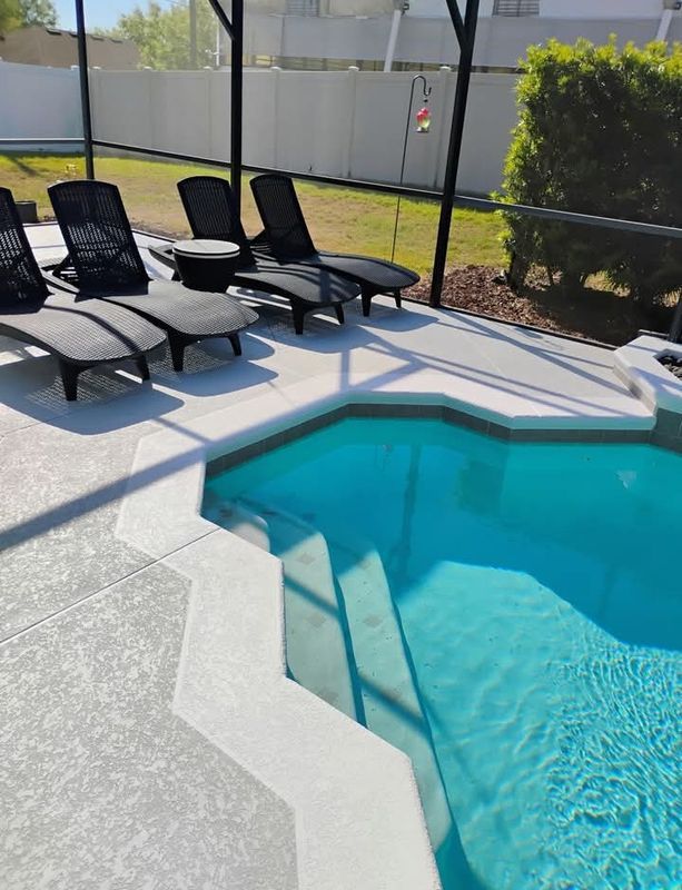 Backyard pool with blue water, lounge chairs, and screened patio beside a concrete deck