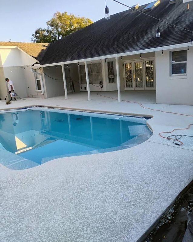 Backyard swimming pool beside a white house with a dark roof and covered patio