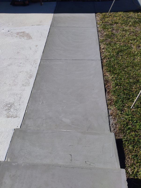 Concrete sidewalk with a curb ramp beside a driveway and grass lawn