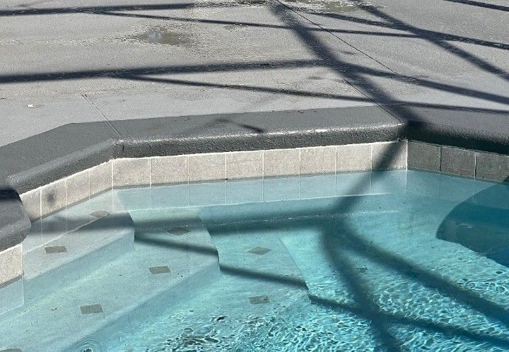 Corner of a turquoise swimming pool with gray stone coping and sunlit shadow patterns.