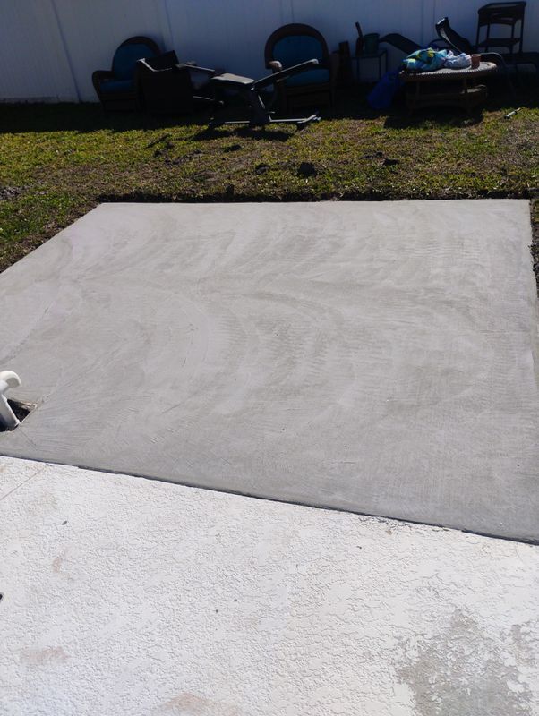 Concrete patio and grassy yard with outdoor chairs against a wall in sunlight