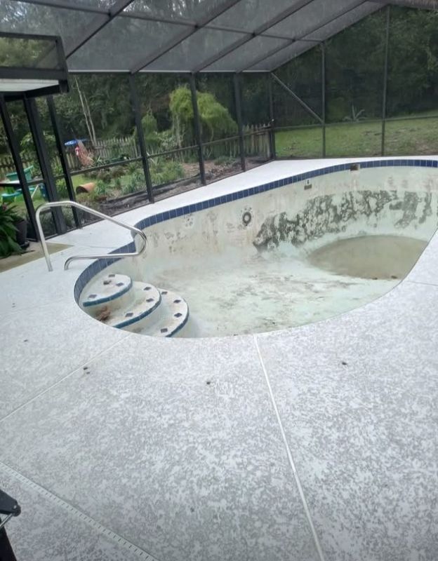 Drained swimming pool with stained concrete, steps, and screened lanai enclosure