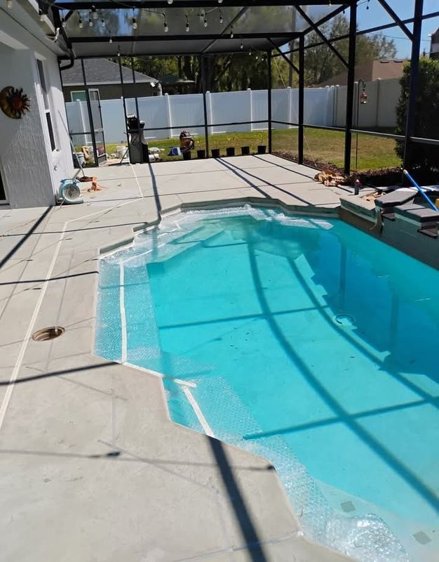 Backyard pool under construction, with bright blue water and a screened patio enclosure