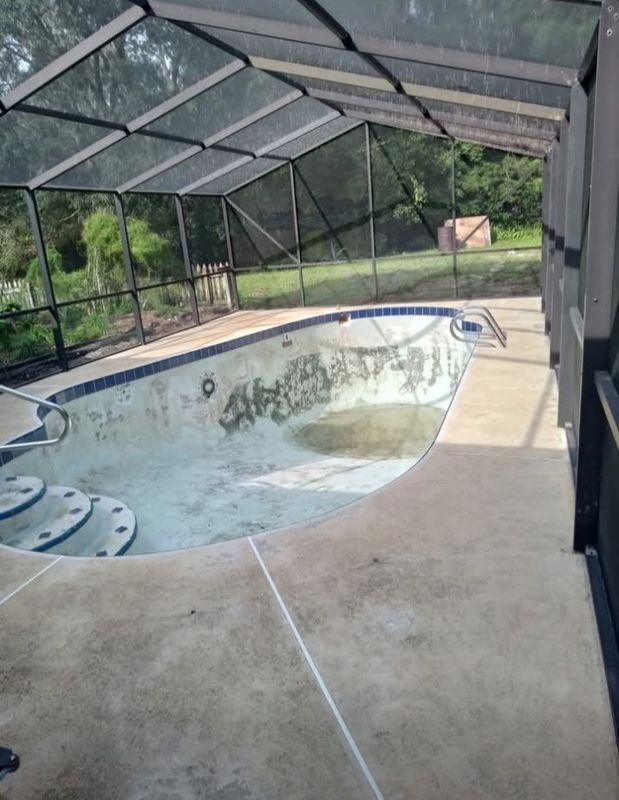 Enclosed backyard pool with cloudy water and a screened patio deck