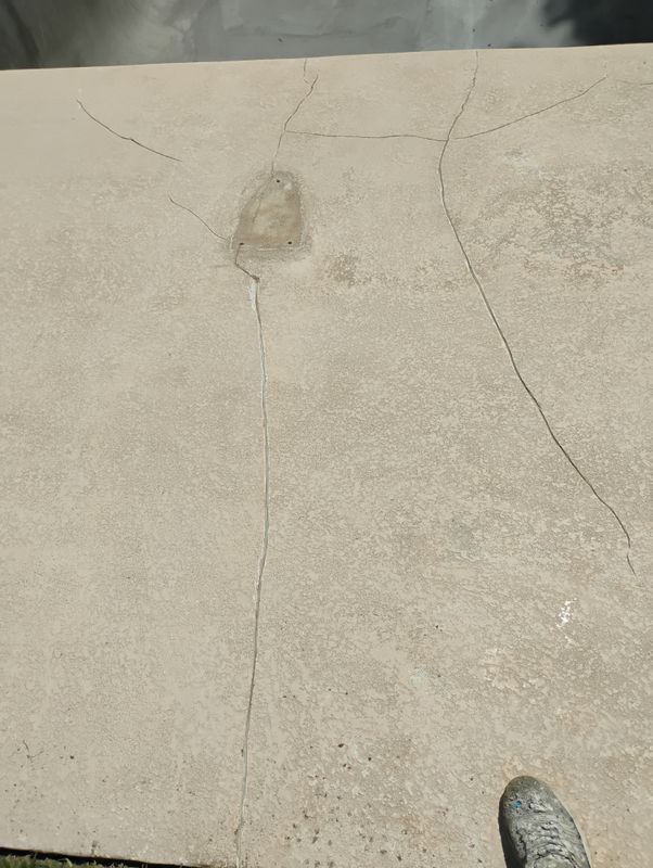 Cracked concrete pavement with a small stain and the tip of a shoe at bottom right