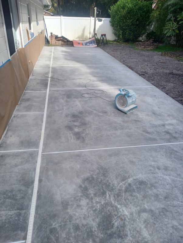 Long concrete driveway under construction with expansion joints and a saw on the ground.