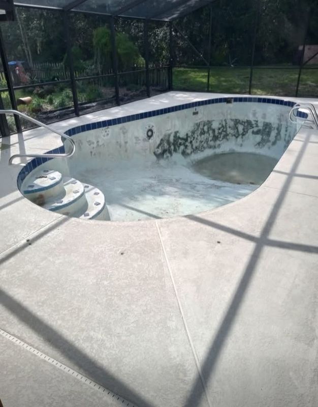 Empty backyard swimming pool with worn blue tile and a concrete deck under a screened enclosure.
