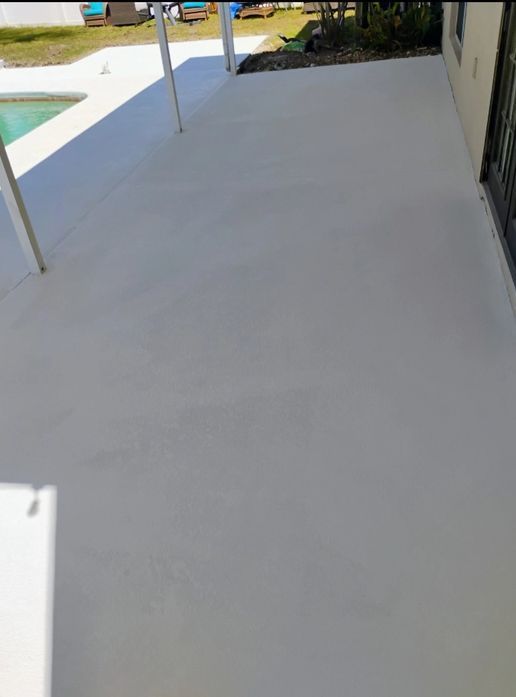 Empty light gray patio beside a pool, with a house wall and railing in the background.