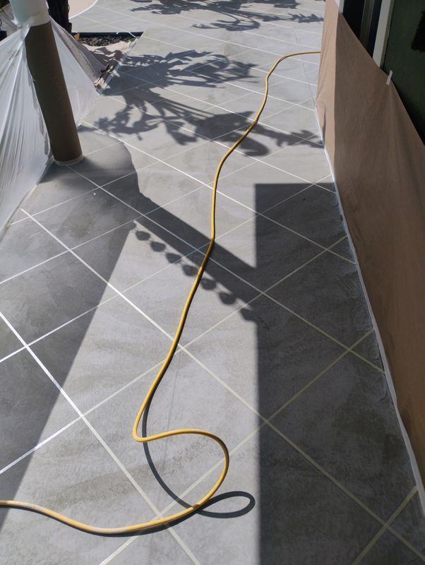 Yellow extension cord lying across a sunlit tiled walkway outdoors, creating a trip hazard.