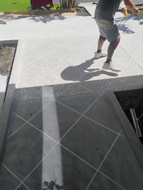 Person walking on a sunlit concrete walkway with a diamond-patterned section in the foreground