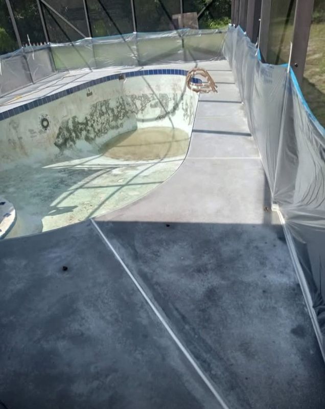 Abandoned backyard pool with peeling white liner and a concrete deck, seen through a safety fence