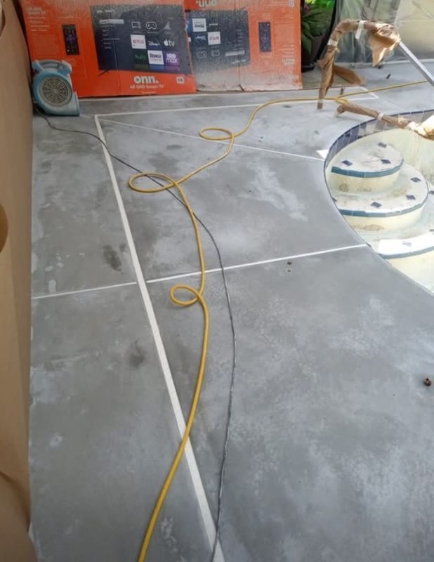 Construction area with concrete floor, yellow cable, orange equipment, and a worker in the background.