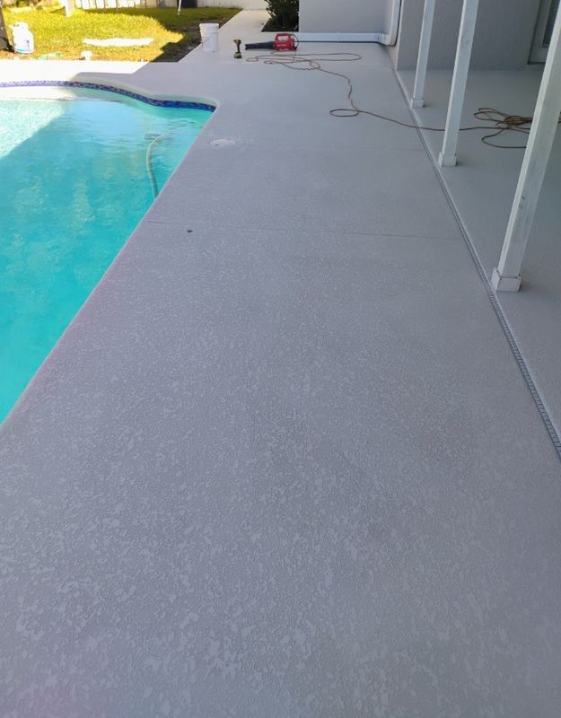 Poolside patio with light gray concrete beside a blue swimming pool and house wall