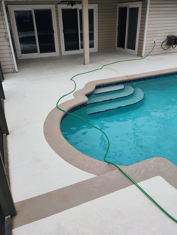 Backyard swimming pool with a green hose on the deck and steps leading into the water