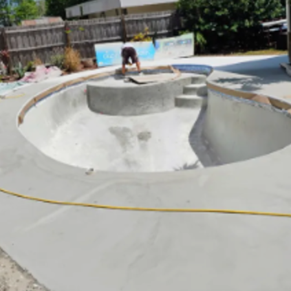 Empty concrete skate bowl with a person working inside on a sunny day.
