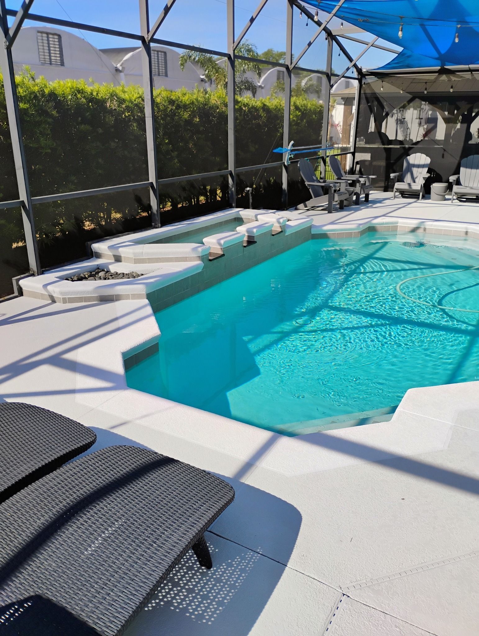 Backyard pool with turquoise water, white deck chairs, and screened enclosure in bright sunlight.