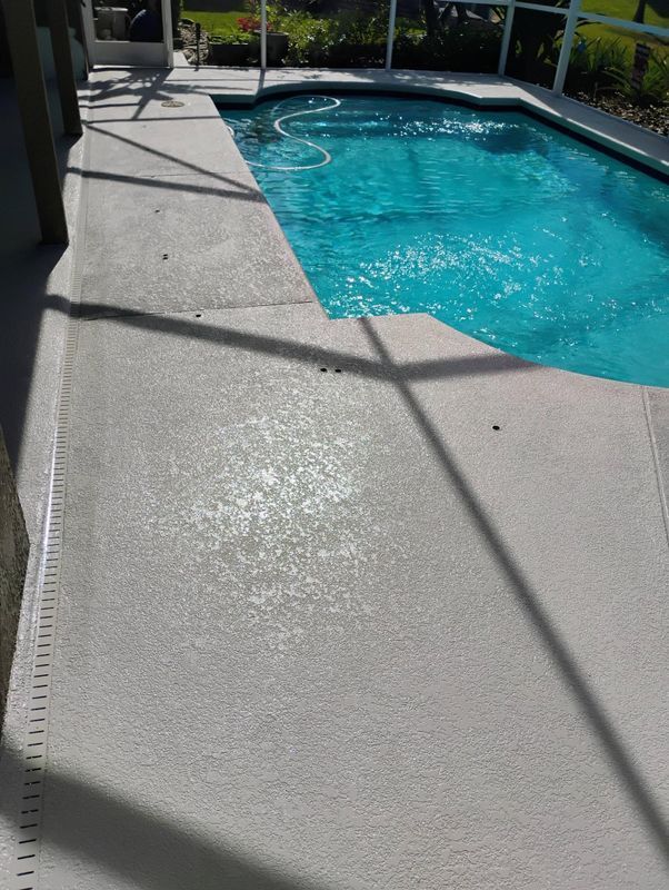 Sunlit concrete pool deck beside a turquoise swimming pool with diagonal shadows.
