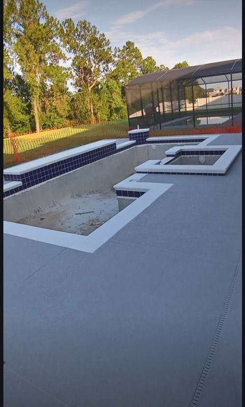 Modern backyard with an empty pool under construction beside a glass-walled patio.