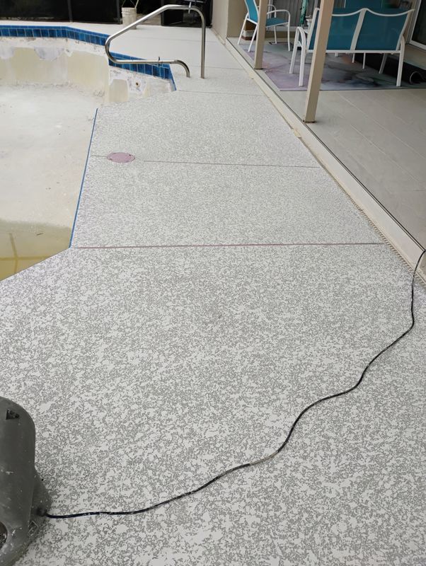 Black cable lying across a speckled walkway beside a pool area.