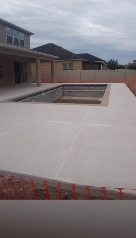 Empty backyard swimming pool beside a house with a concrete deck and fenced perimeter