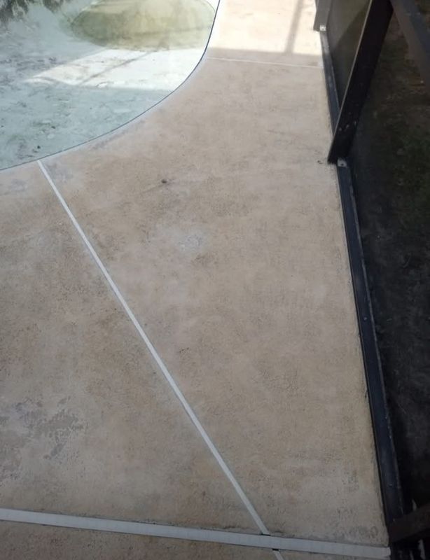Curved concrete walkway beside a glass wall and pool edge