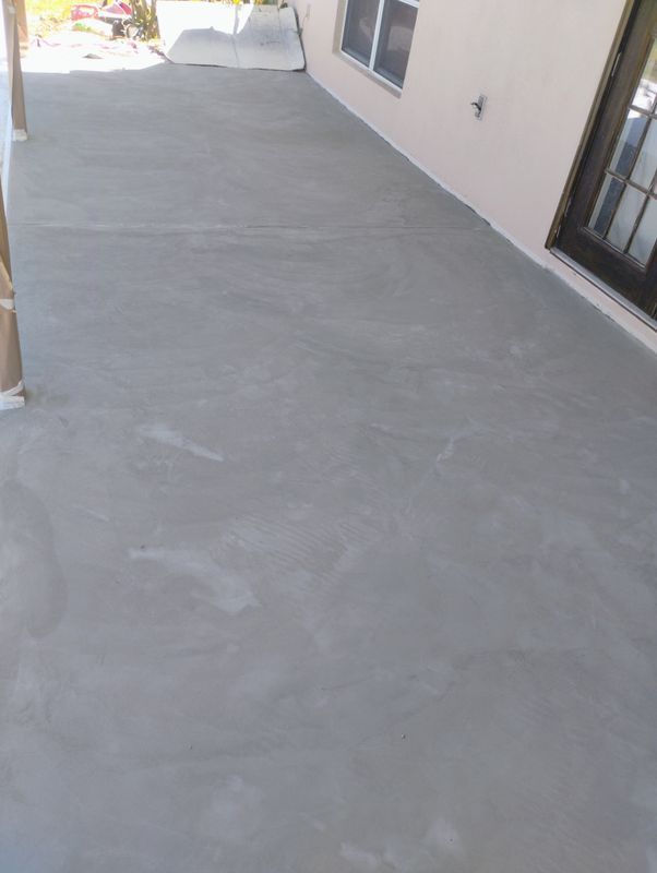 Concrete patio beside a house with a sliding glass door and window, viewed along the wall.