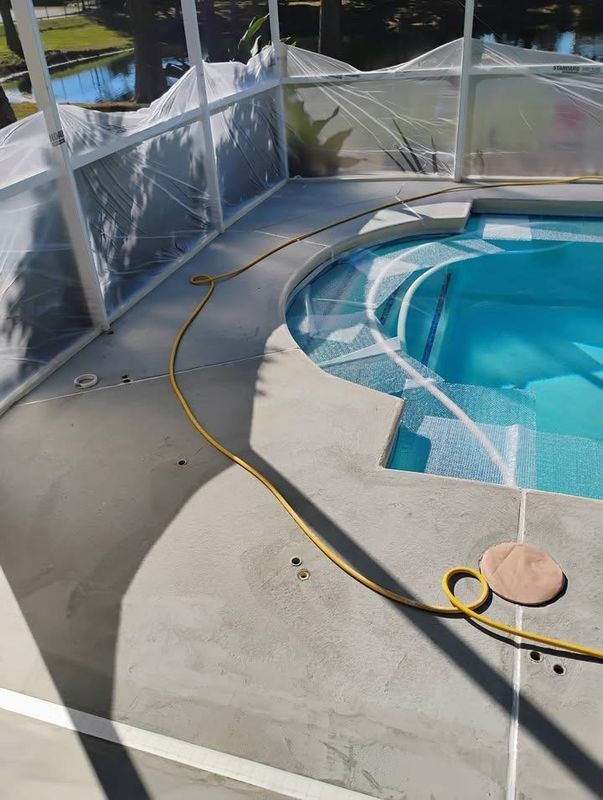 Pool deck with a yellow hose beside a screened swimming pool and concrete patio.