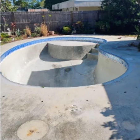 Empty concrete backyard skate bowl with blue rim and central platform in sunlight.