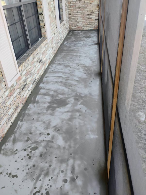 Narrow concrete side yard between brick walls and a screen door, with wet spots on the ground.