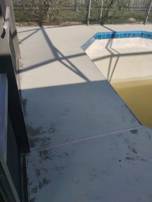 Concrete poolside walkway beside an empty pool with yellow water and blue tile trim.