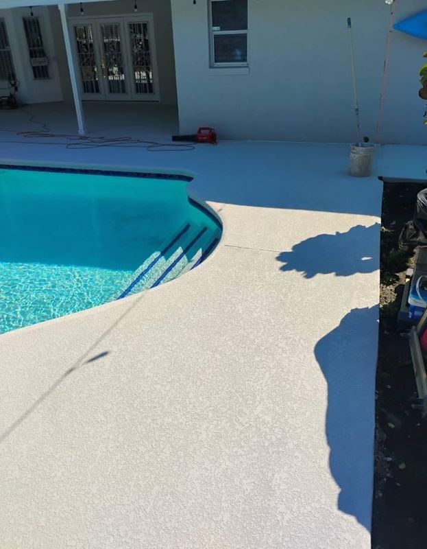 Poolside patio with a light-colored textured deck beside a blue swimming pool and house exterior.