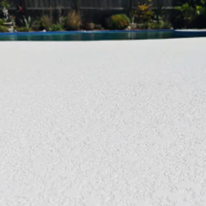 Snow-covered ground beside a blue pool with trees and buildings in the background.