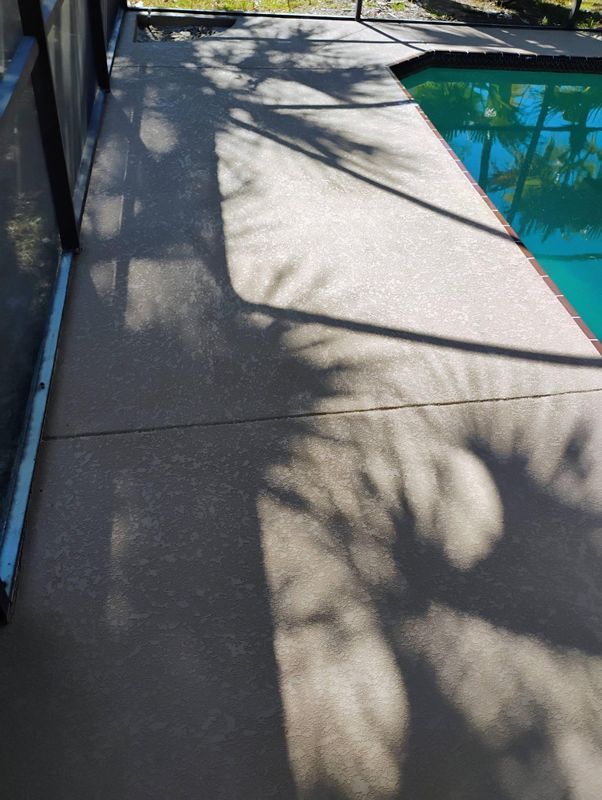 Concrete poolside walkway beside blue water, with tree shadows cast across the ground.