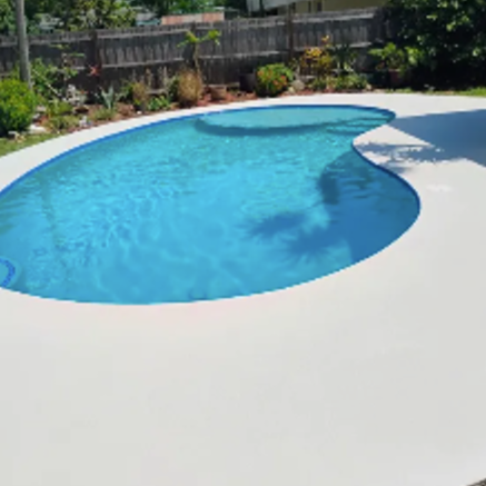 Backyard swimming pool with blue water, white deck, and garden border.