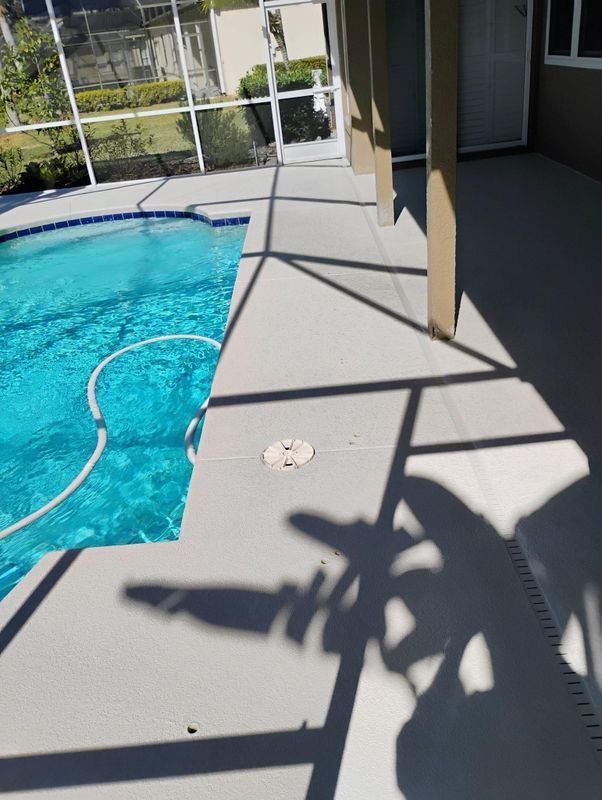 Patio beside a blue swimming pool, with a hose and strong window shadows on the concrete.