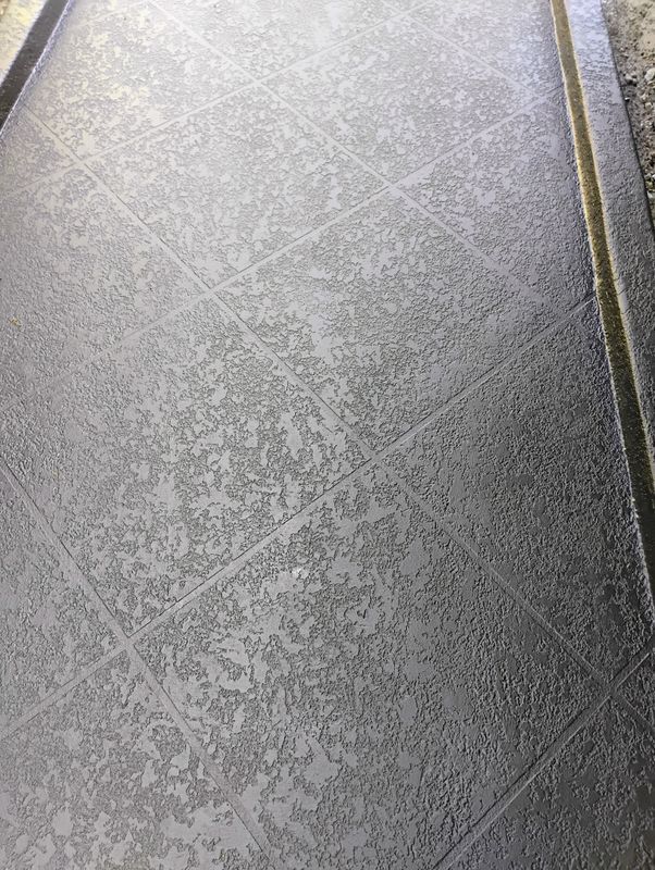 Close-up of gray textured tile flooring with diagonal grout lines and a dark edge on the right.