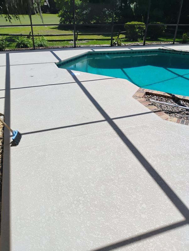 Backyard swimming pool with turquoise water, light concrete deck, and black fence in sunlight.