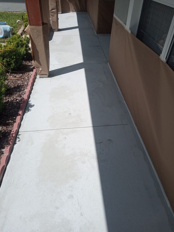 Narrow concrete sidewalk beside a building, bordered by a landscaped strip with red edging.