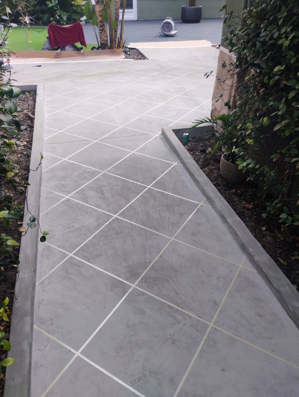 Diagonal gray tiled garden walkway bordered by shrubs and potted plants.