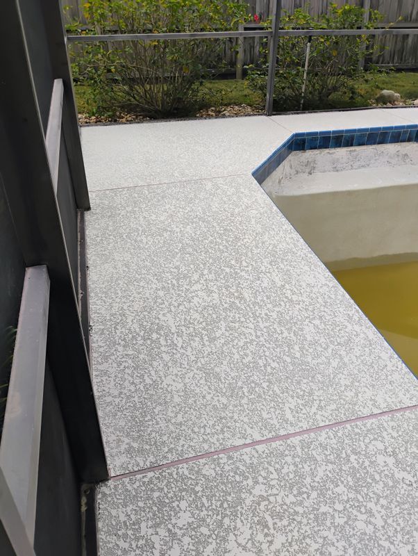 Concrete walkway beside a pool with yellow water, bordered by a black railing and garden fence