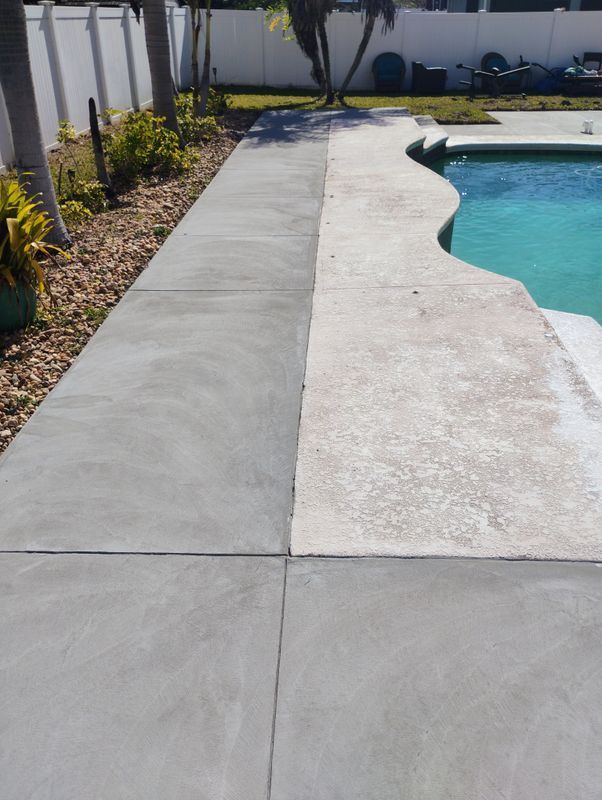 Concrete pool deck with a curved blue swimming pool and landscaped walkway beside a wall.