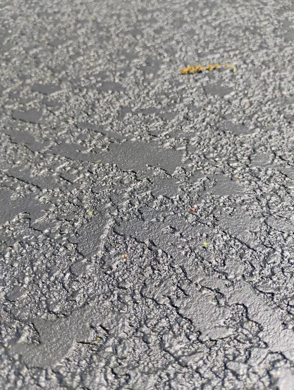 Close-up of cracked gray pavement with a small yellow leaf near the top.