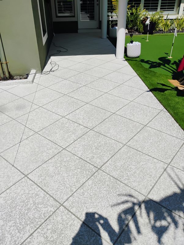 Light gray tiled patio leading to a house entrance beside a green lawn and white planter.