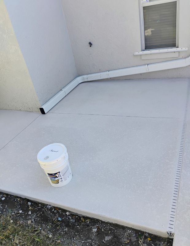 White patio surface with a paint bucket near a house wall and window.