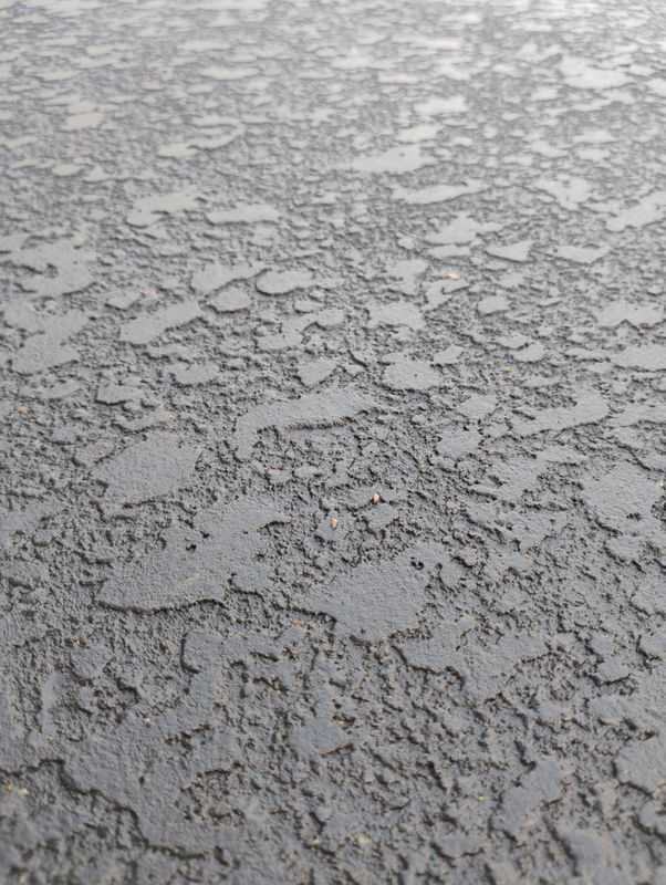 Close-up of wet gray textured pavement with scattered puddles.