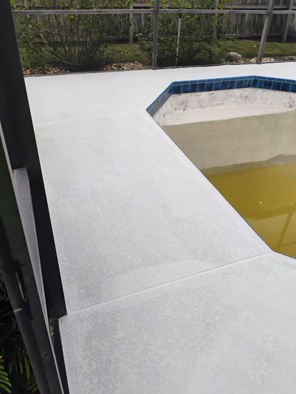 White pool deck beside a yellow-tinted hot tub with blue tile edging, next to a fenced outdoor area.