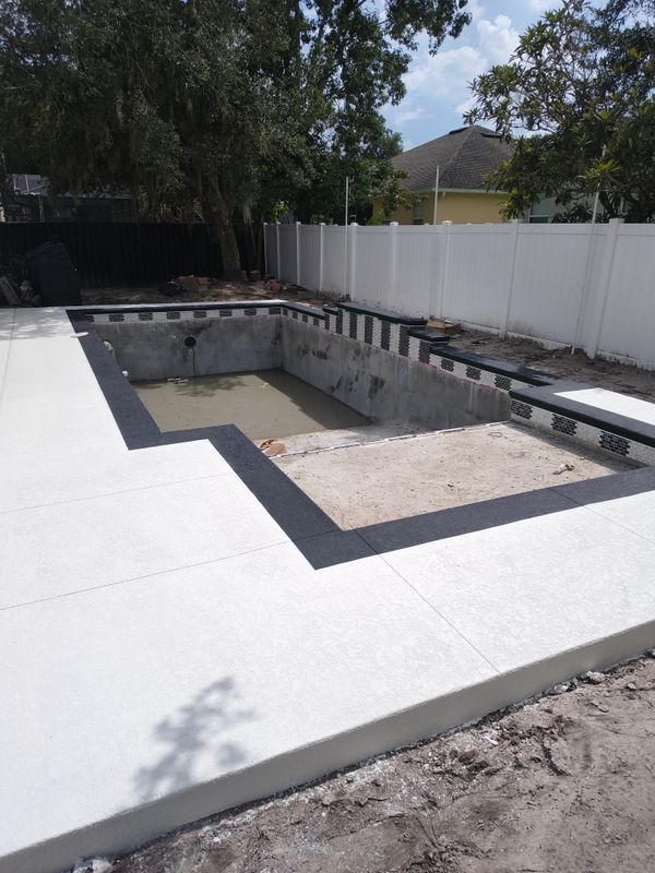 Partially built backyard pool with white deck and white privacy fence.