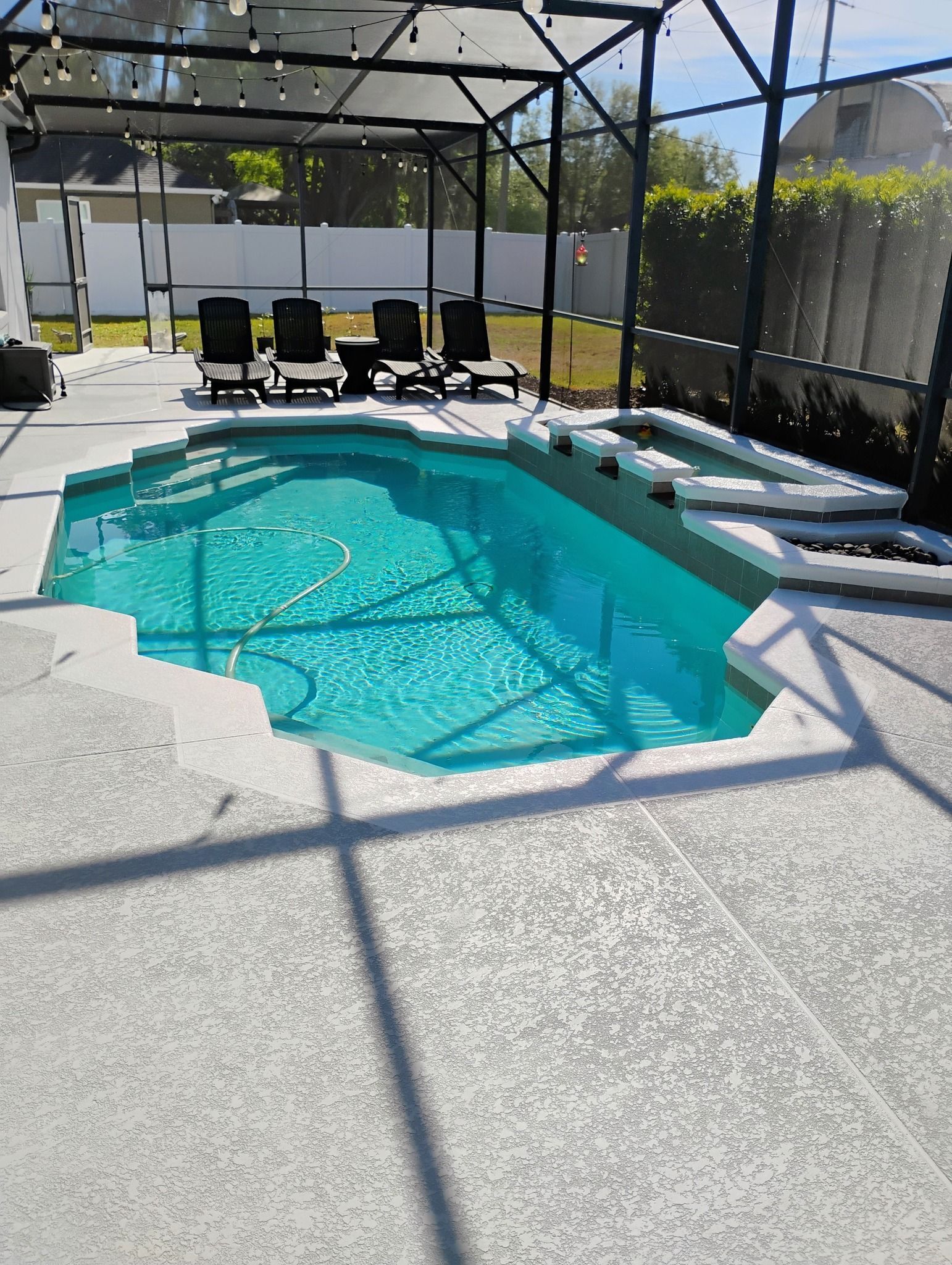 Screened backyard pool with turquoise water, white deck, and lounge chairs in bright sunlight